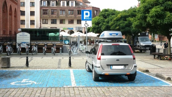 Samochód zaparkowany na niebieskiej tzw. kopercie. Obok pusta druga koperta, w tle miejska zabudowa