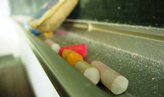 Kolorowe kawałki kredy i gąbka leżą pod szkolną tablicą