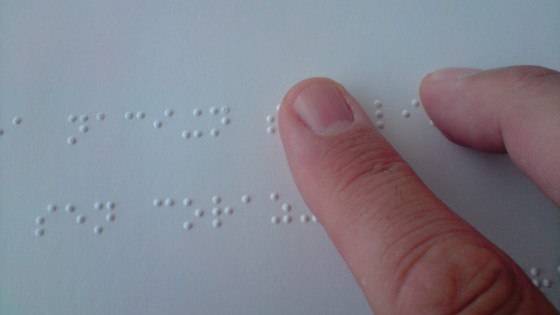 Palce dotykające wypukłych punktów alfabetu Braillea