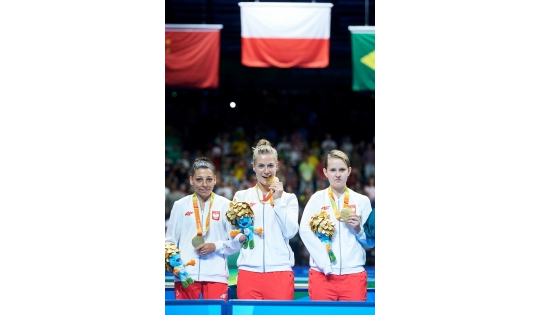 Trzy reprezentantki Polski z medalami. Nad nimi najwyżej wisi polska flaga, obok flagi Chin i Brazylii